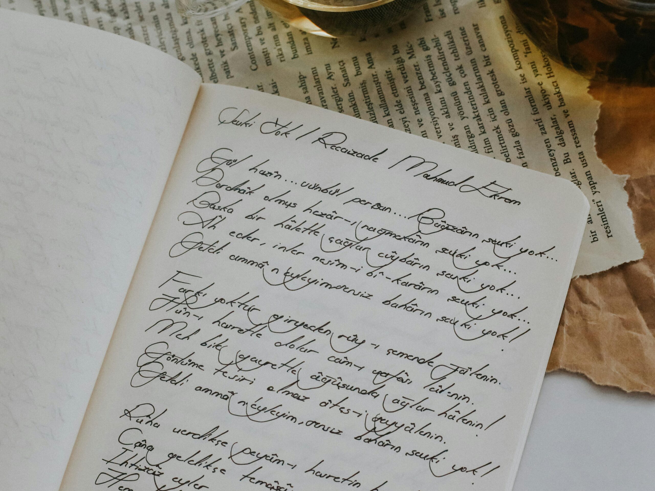 Open notebook with handwritten poem, tea, and newspaper. Cozy and creative concept.