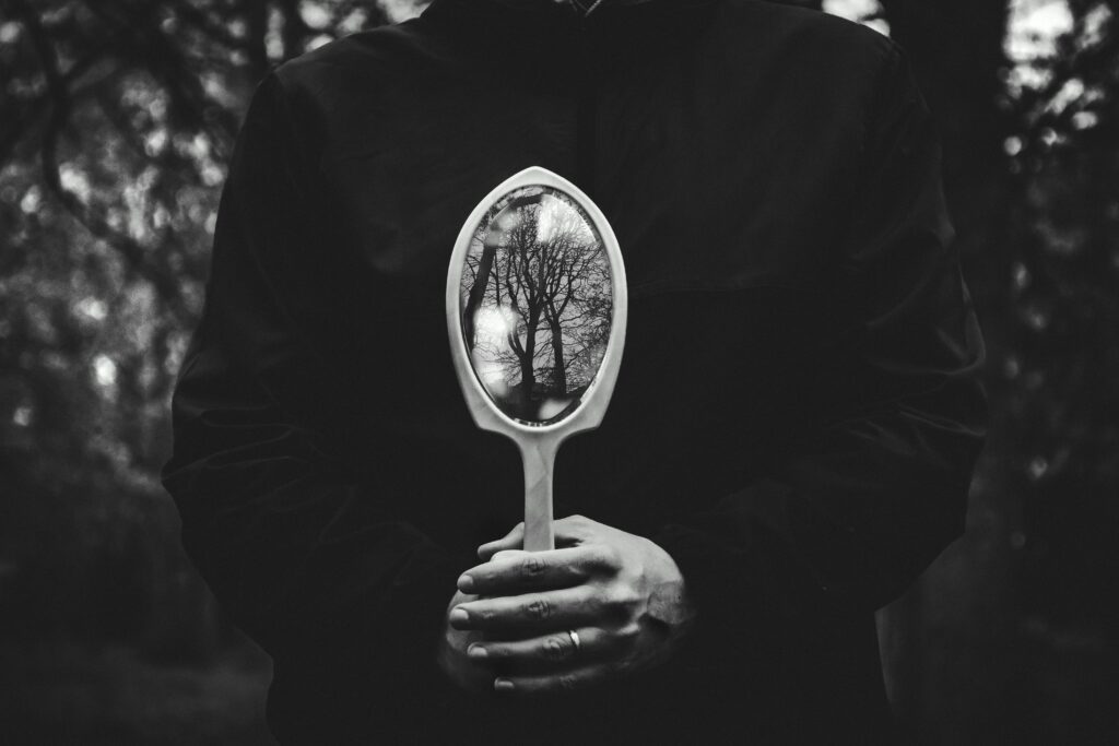 A person holding a mirror reflecting bare trees in a black and white setting.